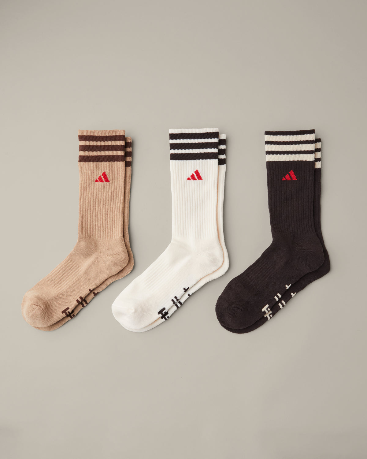 Three pairs of women’s adidas® crew socks in tan, cream, and espresso brown with striped cuffs and red adidas® logos. - Image #1