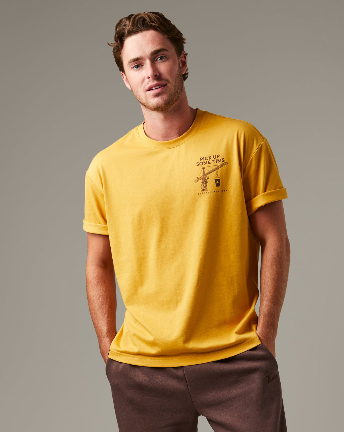 Ochre Tim Hortons crew-neck T-shirt with a small Pick Up Some Tims crane and coffee cup graphic on the chest. | T-shirt Tim Hortons ocre à encolure ronde avec une petite illustration de grue et de gobelet de café « Prendre son Tim » sur la poitrine.