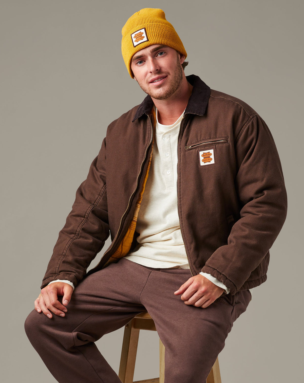 Espresso-brown Tim Hortons workwear jacket with a dark collar, front zipper, zippered chest pocket, side pockets, and retro logo patch. | Veste de travail Tim Hortons brune espresso avec col foncé, fermeture à glissière sur le devant, poche poitrine à fermeture à glissière, poches latérales et écusson à logo rétro.