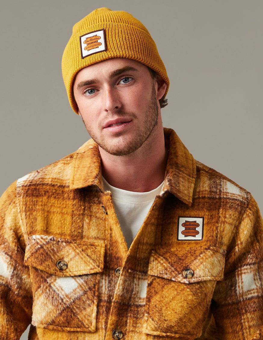 Yellow, brown, and cream plaid Tim Hortons shacket with a button front, two flap chest pockets, and a small logo patch. | Surchemise Tim Hortons à carreaux jaunes, bruns et crème, avec fermeture à bouton sur le devant, deux poches poitrine à rabat et un petit écusson à logo.